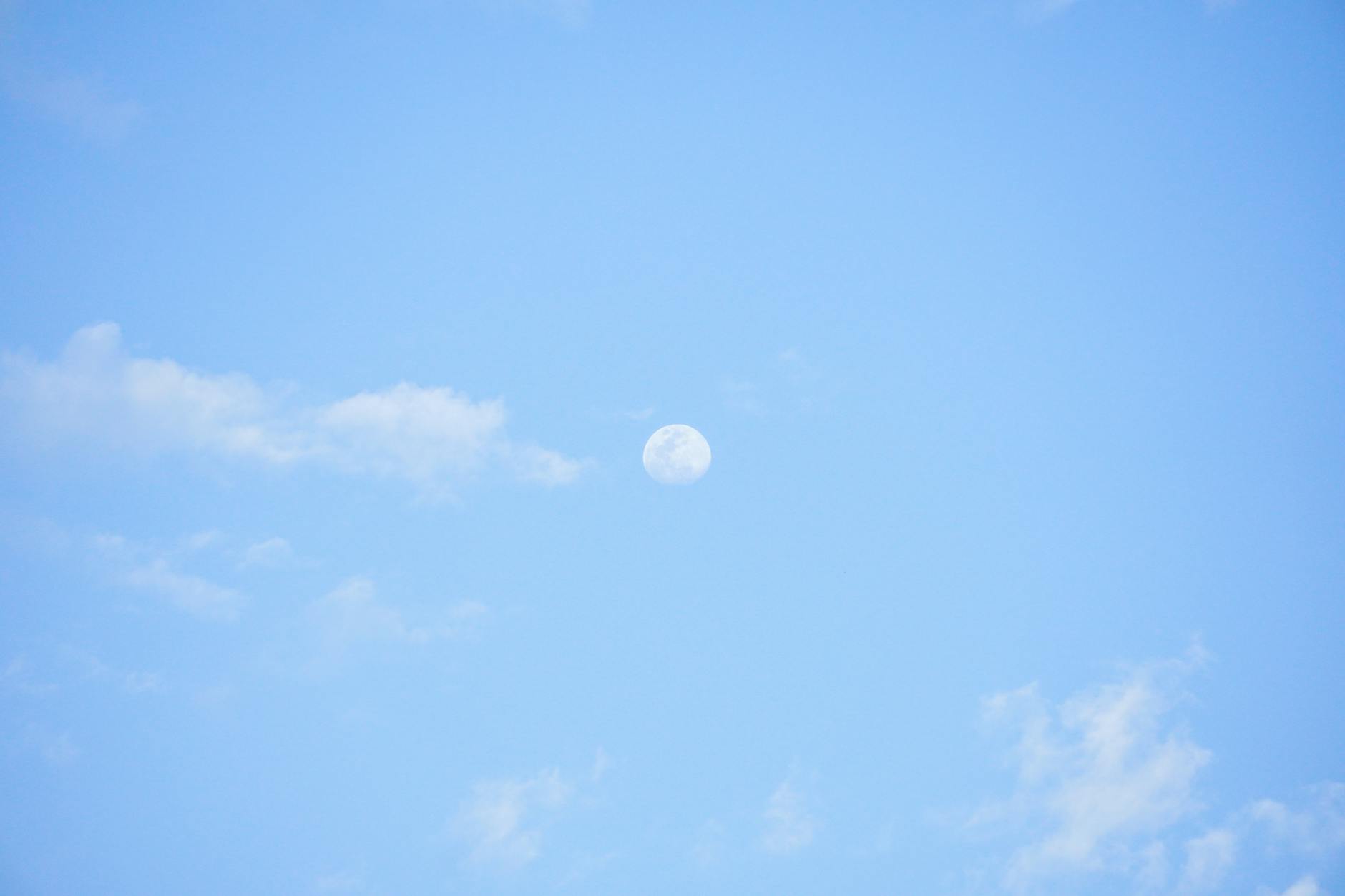 Błękitne dzienne niebo z widocznym księżycem i jasnymi chmurami