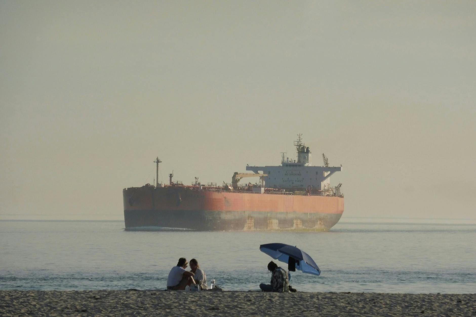 Tankowiec z ropą zakotwiczony blisko plaży z wypoczywającymi ludźmi