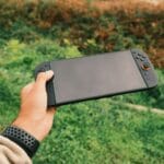 Dłoń trzymająca czarną konsolę przenośną na tle zieleni