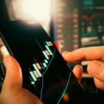 Dłonie analizujące wykresy finansowe na ekranie smartfona