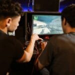 Dwóch młodych mężczyzn gra w arcade’ową grę MMO na automatach