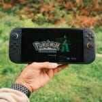 Dłoń trzyma konsolę przenośną z grą Pokémon Legends na ekranie